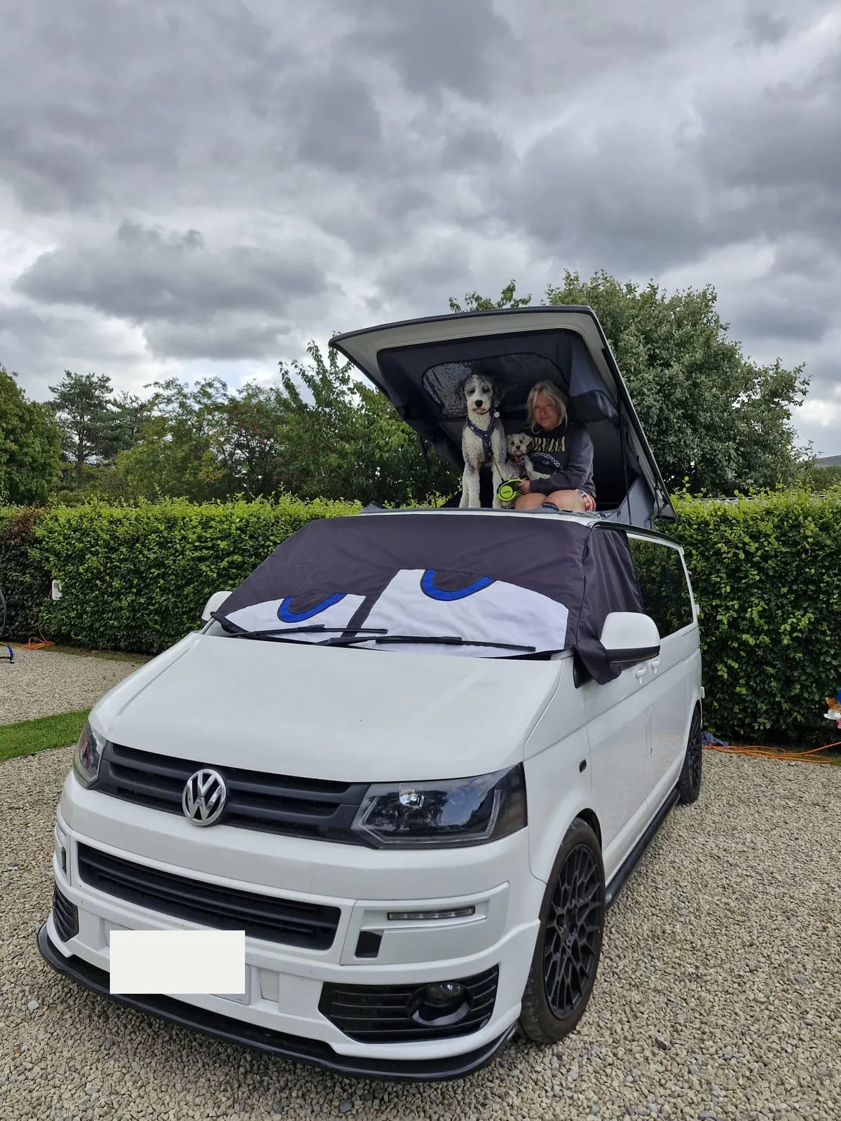 White Volkswagen Transporter campervan converted by Potteries Camper Co with its pop-top roof raised and the upper bed in use