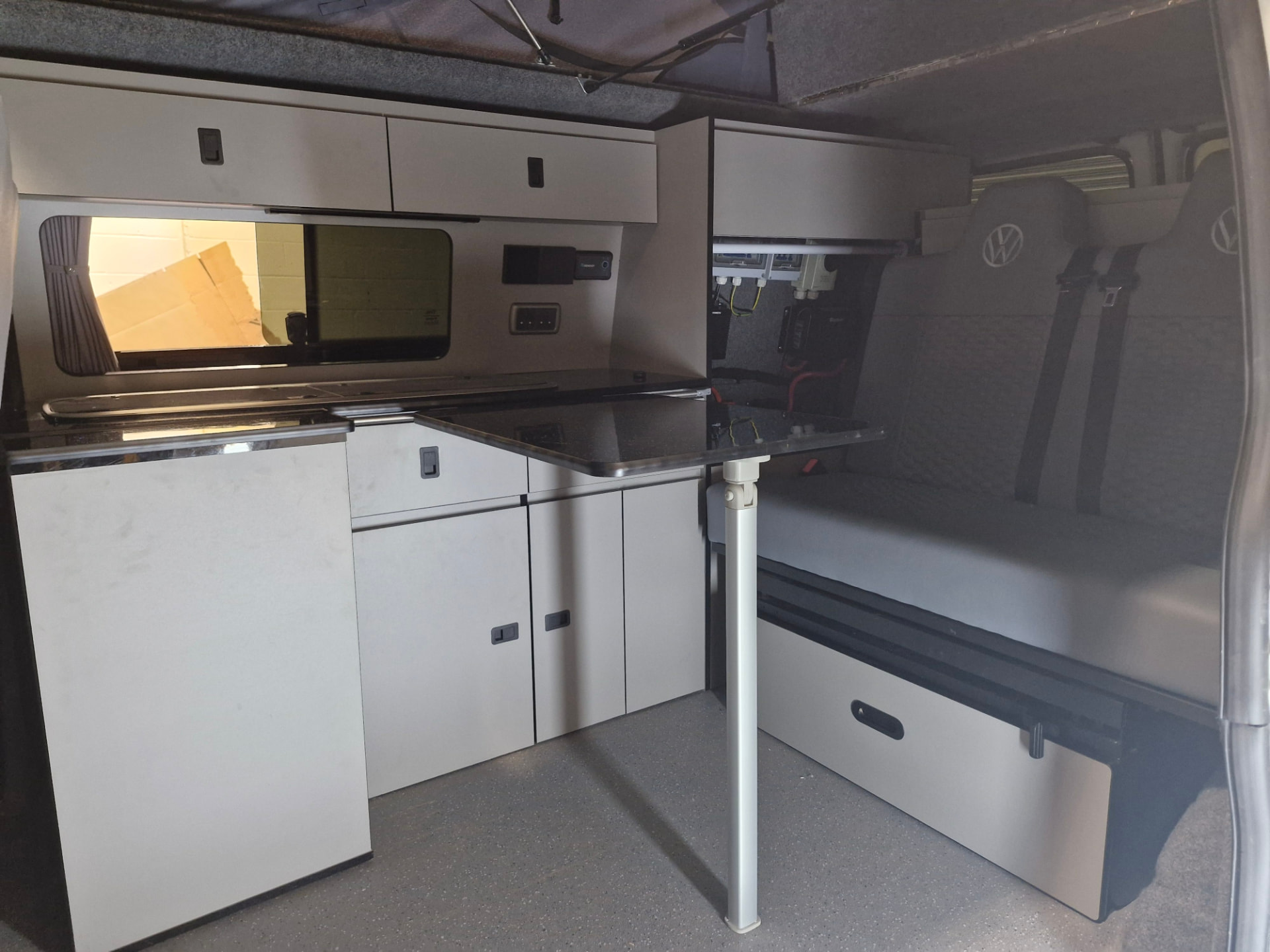 Campervan interior with grey kitchen furniture, overhead lockers, pull-out table and rear seating